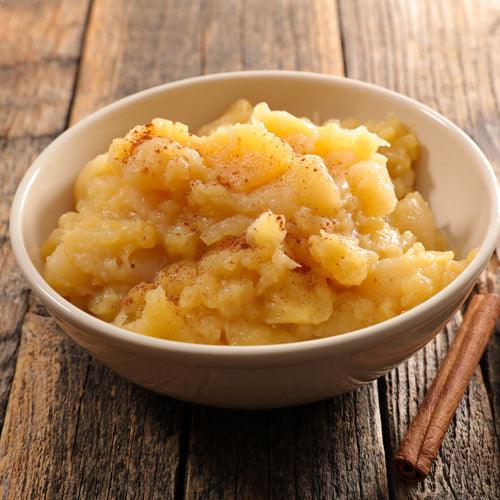 Homemade cinnamon applesauce in a glass jar with fresh apples, cinnamon sticks, and cozy fall background