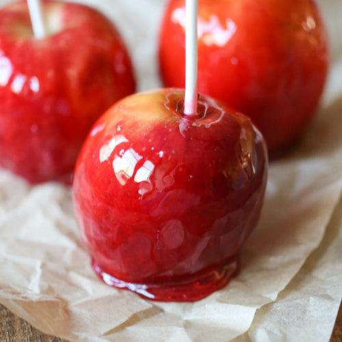 Cinnamon roll candy apples on parchment paper with caramel coating, cinnamon sugar, and white chocolate drizzle