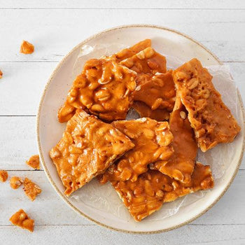 Homemade nutty brittle broken into golden caramel shards with roasted peanuts and almonds on parchment paper